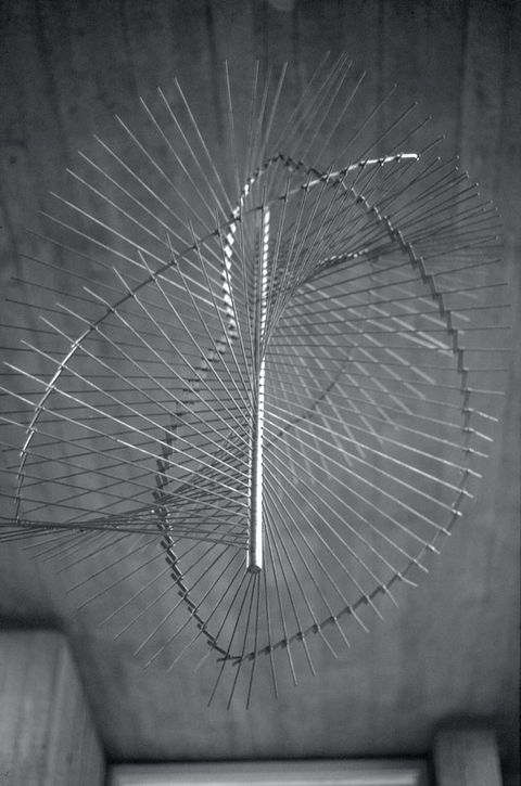 Metal sculpture. Mobile consists of a central vertical bar with hundreds of thin metal rods extending out in all directions to create an interlocking spiral wave.